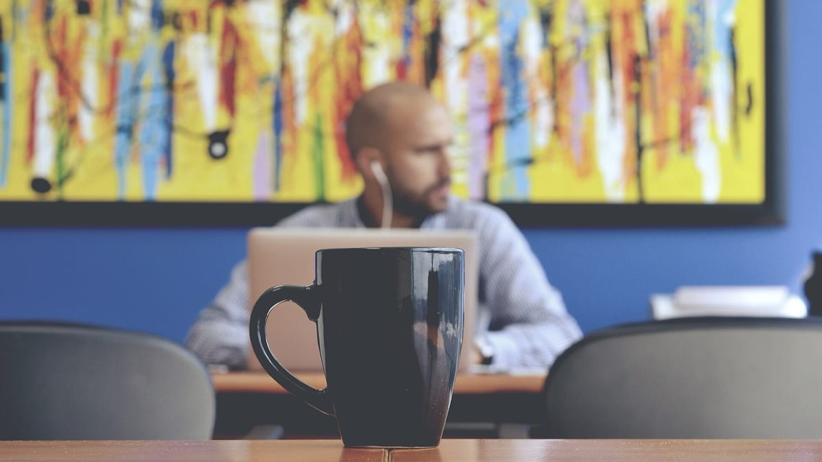 A coffee mug on a table in front of a man working at a laptop